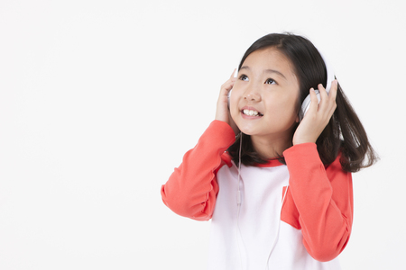 Asian female child listening music isolated on whiteの写真素材