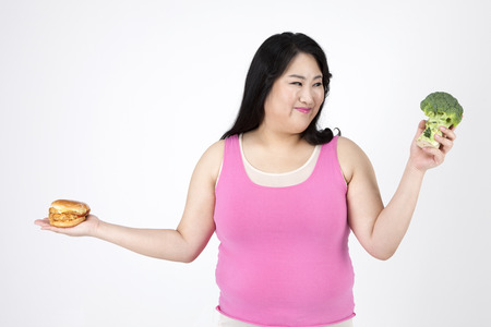 Asian overweight woman choosing vegetable or hamburger isolated on whiteの写真素材
