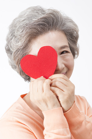 Asian old aged woman with heart shape cutout isolated on whiteの写真素材
