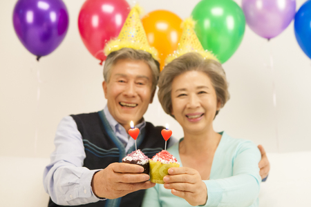 Asian old aged couple celebrating with cupcake isolated on whiteの写真素材