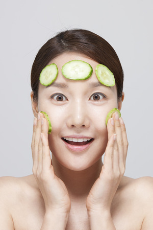 Asian young woman putting cucumber on her face isolated on whiteの写真素材