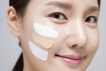 Asian young woman with tube foundation on face isolated on whiteの写真素材