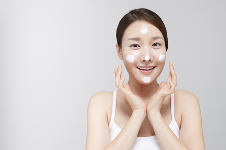 Asian young woman applying cream on face isolated on whiteの写真素材