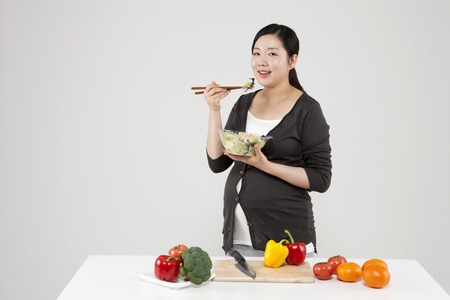 Asian pregnant woman eating fresh food isolated on whiteの写真素材