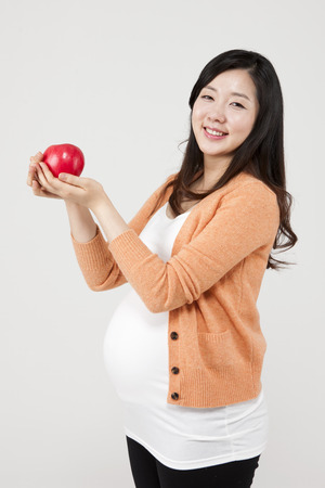 Asian pregnant woman with apple isolated on whiteの写真素材