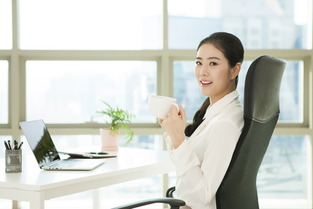 Asian working woman drinking coffee on the desk in officeの写真素材