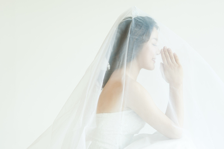 Asian beautiful bride in wedding veil praying isolated on whiteの写真素材