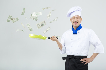 Asian male chef cooking paper money with pan isolated on whiteの写真素材