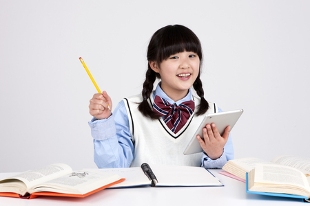 Asian elementary school girl using tablet pc with pencil isolated on whiteの写真素材