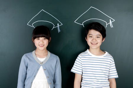 Graduation hat against Asian boy and girl with smile at blackboardの写真素材