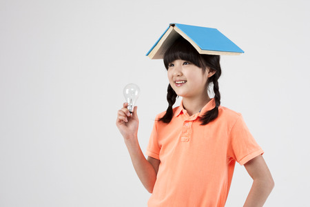 Asian elementary school girl with book and light bulb isolated on whiteの写真素材