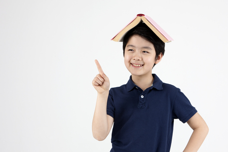 Asian elementary school boy with book on his head isolated on whiteの写真素材