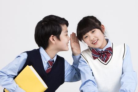 Asian elementary school students whispering isolated on whiteの写真素材