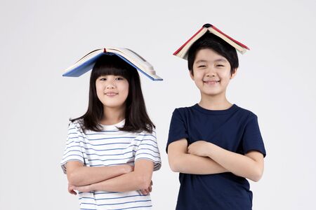 Asian elementary school students with book on their head isolated on white