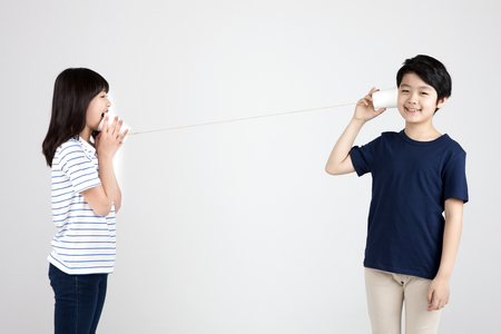 Asian elementary school students with paper cup phone isolated on whiteの写真素材