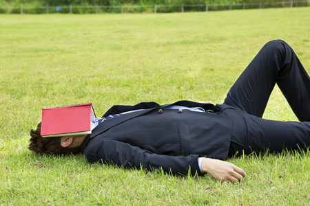 Asian young man in suit lying on the grass outdoorの写真素材