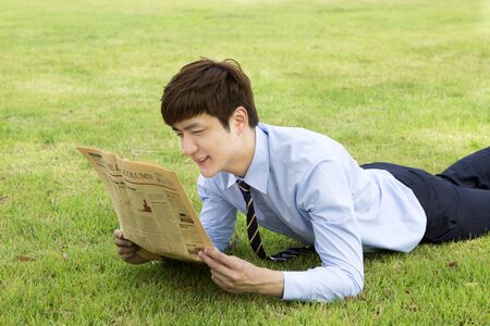 Asian man in suit reading newspaper on grassの写真素材