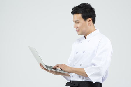 Asian male chef using laptop isolated on whiteの写真素材