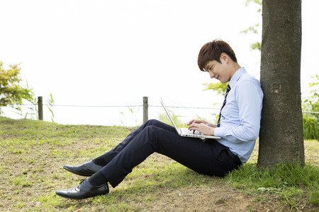 Asian man in suit using laptop on grass outdoorの写真素材