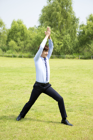 Asian man in suit doing Pilates on grassの写真素材