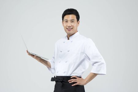 Asian male chef using laptop isolated on whiteの写真素材