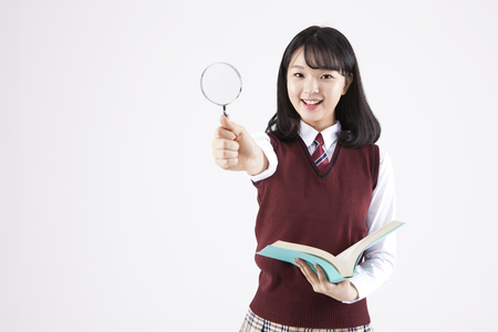 Asian female high school student with magnifier and book isolated on whiteの写真素材