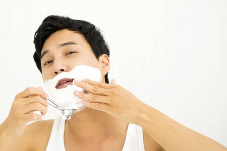 Asian young man shaving in the morning isolated on whiteの写真素材