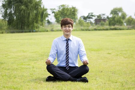 Asian man in suit meditating on grassの写真素材