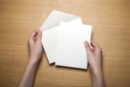 Hand holding white envelope and folded letter on wooden tableの写真素材