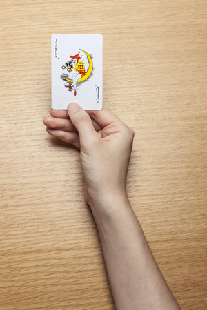 Hand holding joker playing cards wooden tableの写真素材