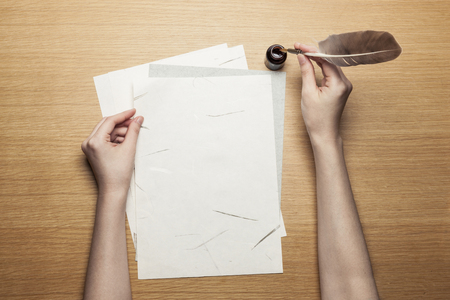 Hand writing on pattern paper with feather quill on wooden tableの写真素材