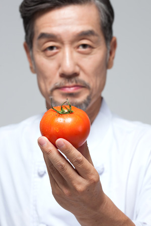 Asian man chef with tomato isolated on whiteの写真素材