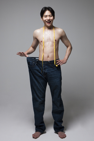 Asian fitness man losing weight isolated on grayの写真素材