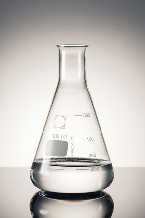 An erlenmeyer flask filled with transparent solution stands isolated on grey background.の写真素材