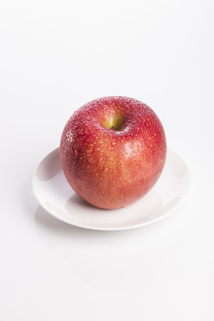 A red ripe apple on a white dish isolated on white backgroundの写真素材