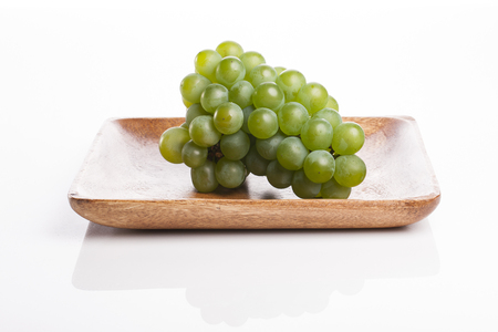 Green grapes on a brown tray isolated on white backgroundの写真素材