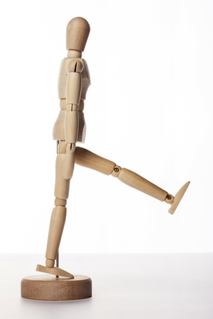 A wooden ball-jointed doll isolated on white background shows a person standing to the side with left leg up.の写真素材