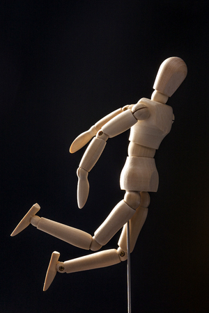 A wooden ball-jointed doll isolated on black background shows a person long jumping to the side.の写真素材