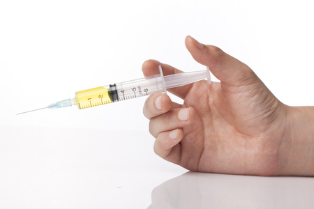 A laboratory syringe filled with yellow solution on white background is held by a right hand.の写真素材
