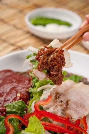Korean cold noodle makguksu with various vegetables and spicy seasoning, picked with chopsticks, close-up shotの写真素材