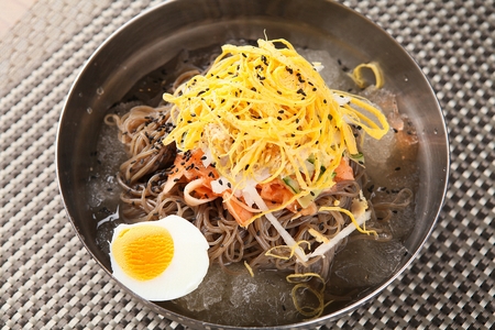 Korean cold noodle makguksu with various vegetables and spicy seasoning, close-up shotの写真素材