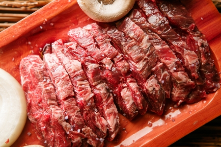 Korean barbecue, raw beef neck chain with vegetables on wooden plate, close-up shot