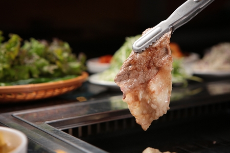 Korean barbecue, assorted beef parts held using tongsの写真素材