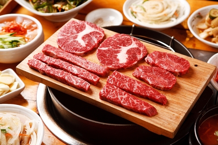 Korean barbecue, raw assorted beef parts on wooden plate along with side dishesの写真素材