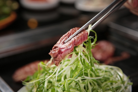 Korean barbecue, assorted beef parts and leek held with chopsticksの写真素材