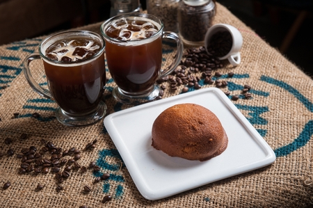 bun on white plate, two glasses of iced black coffee