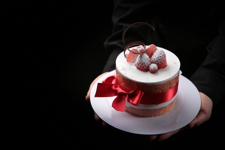 tall strawberry cream cake with starberries and chocolate on top, being served with two hands, black...