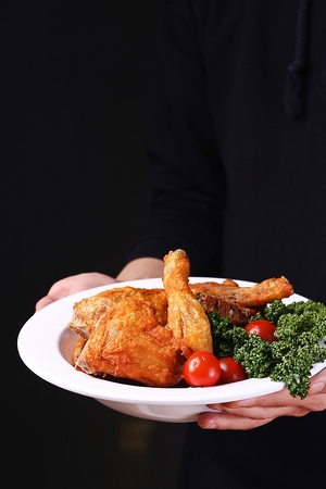 fried chicken with garnish served with two hands, black backgroundの写真素材