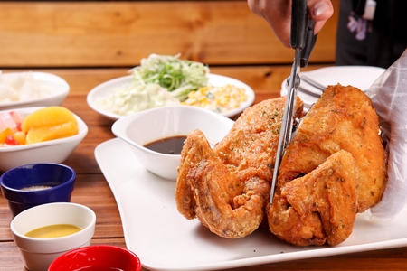 whole fried chicken being halved using scissors, served with salad and various dipping saucesの写真素材