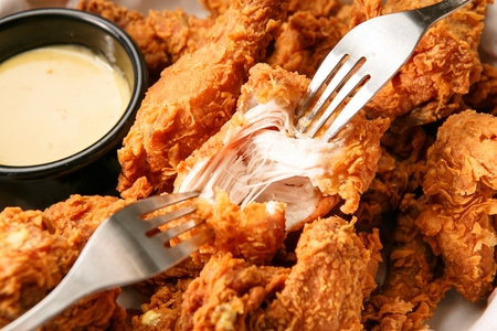 close-up shot of fried chicken, a piece being cut with two forks, honey mustard sauce